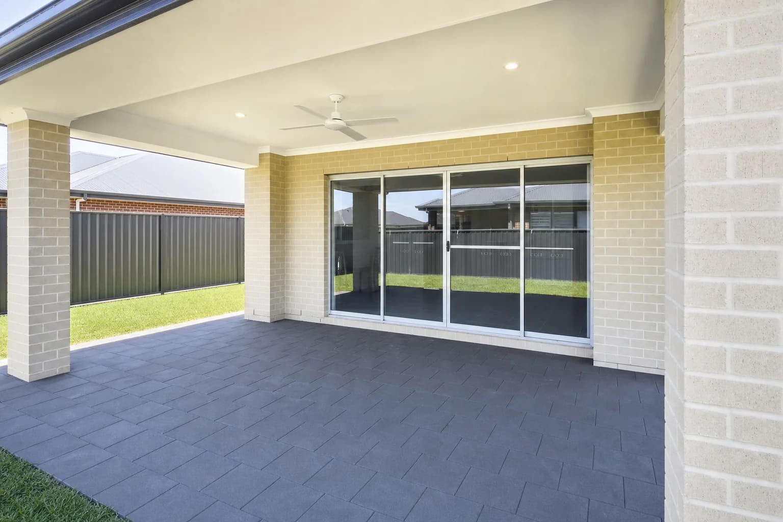 An empty paved alfresco under the main roof of a Perth house, sliding doors closed
