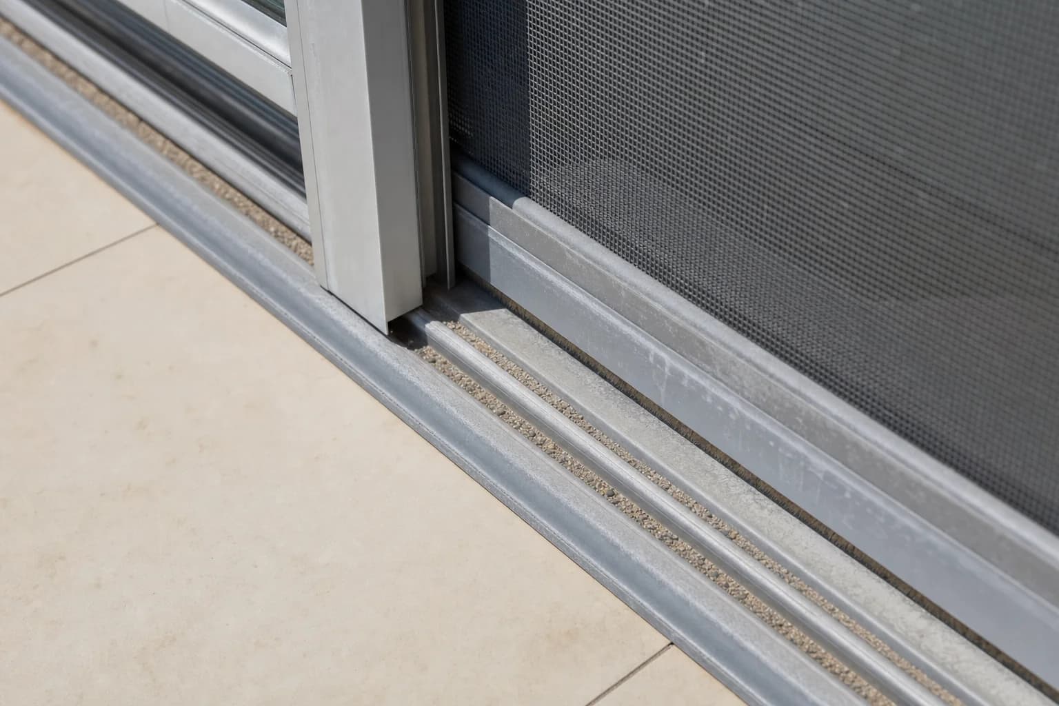 Salt haze and wind-blown sand caught in the bottom track of a sliding door on a coastal Perth property