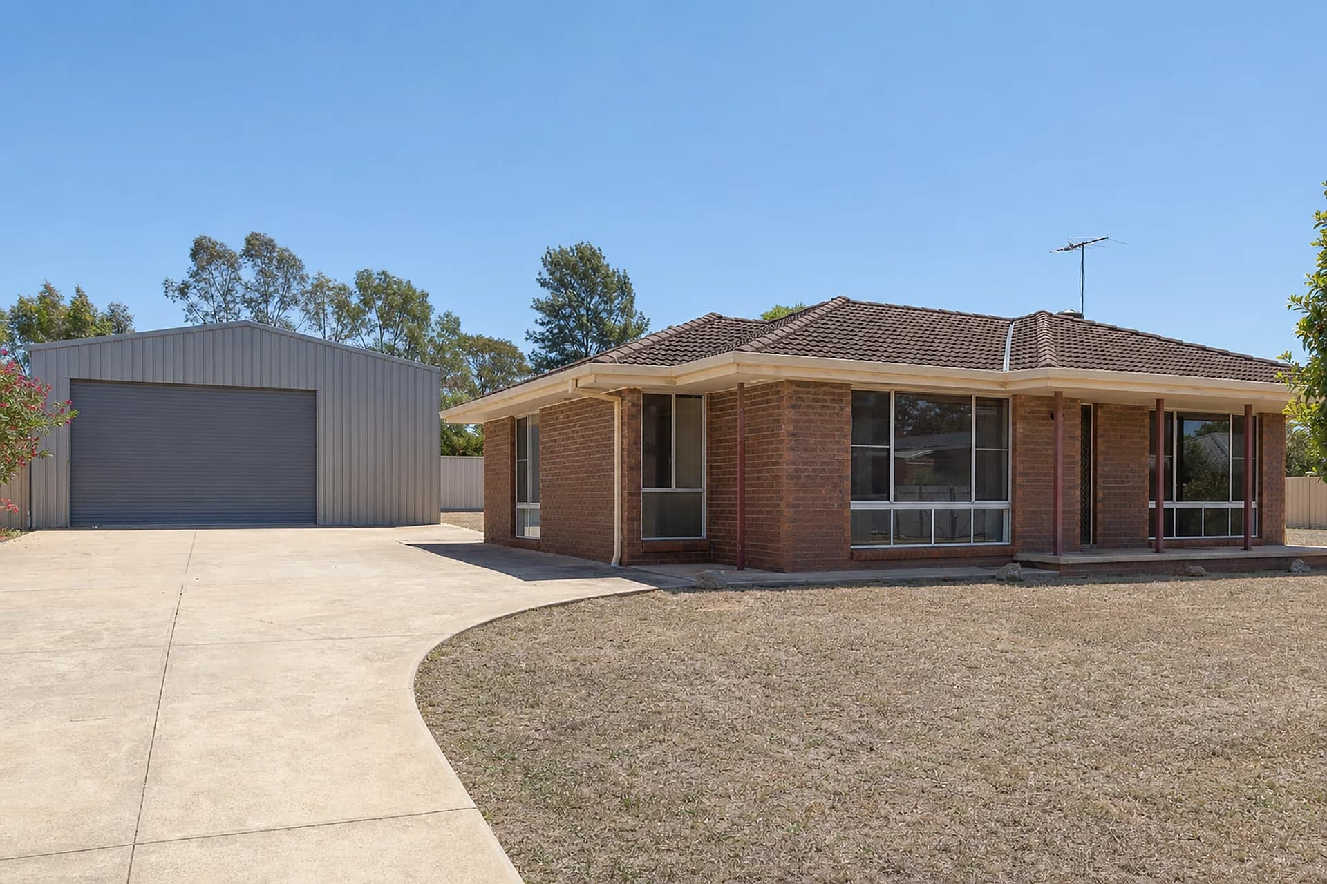 An empty 1970s brick house in Maddington with a large Colorbond shed and concrete hardstand behind it