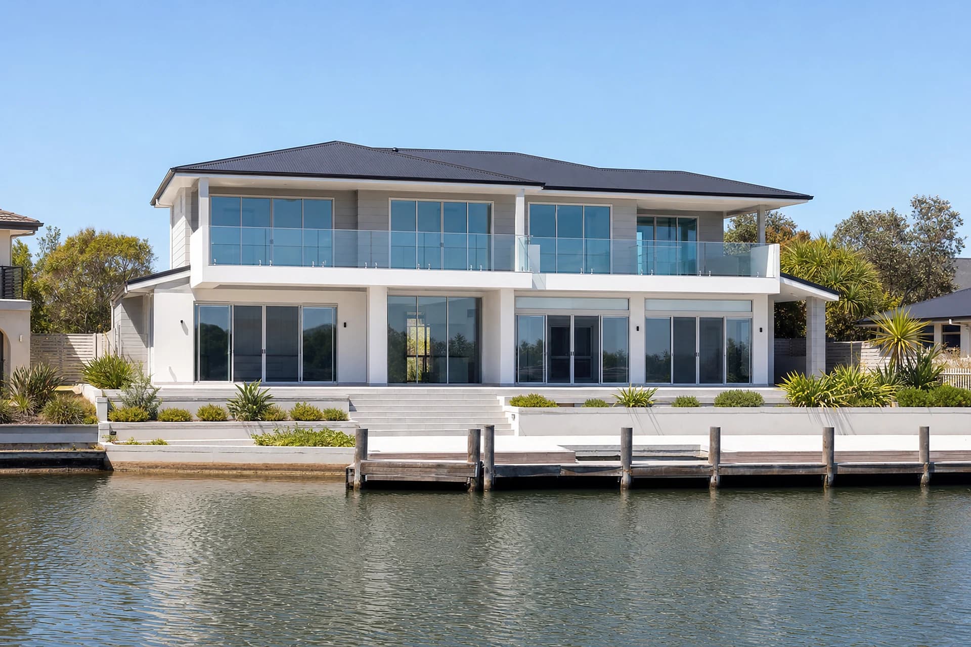 An empty two storey Mandurah canal home seen from the water, glass across both levels and a private jetty