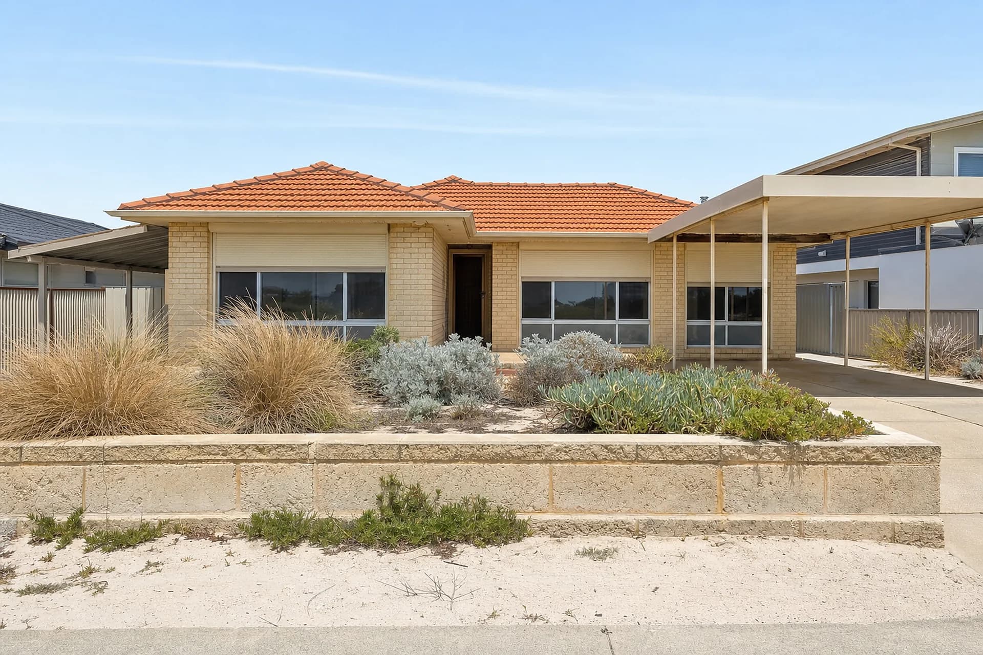 An empty 1980s coastal brick home in Waikiki with roller shutters and a limestone front wall, ready for a vacate clean